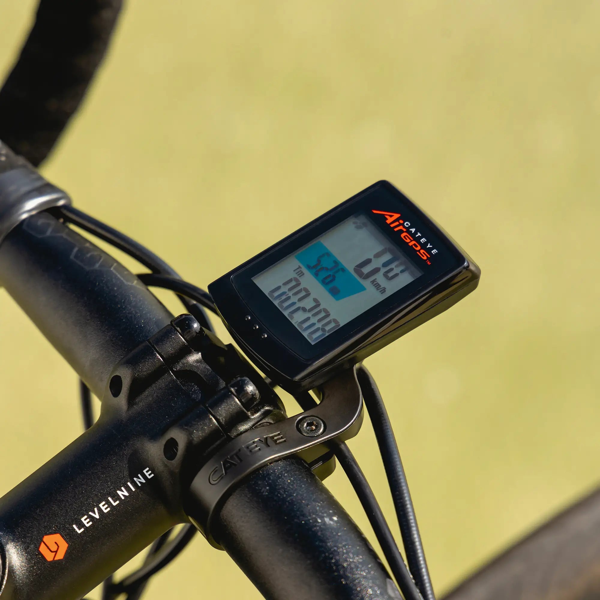 A close-up of a CATEYE AirGPS digital bike computer on a black LEVELNINE handlebar, showing speed, distance, and riding metrics with precise GPS. The LEVELNINE label is partially visible.