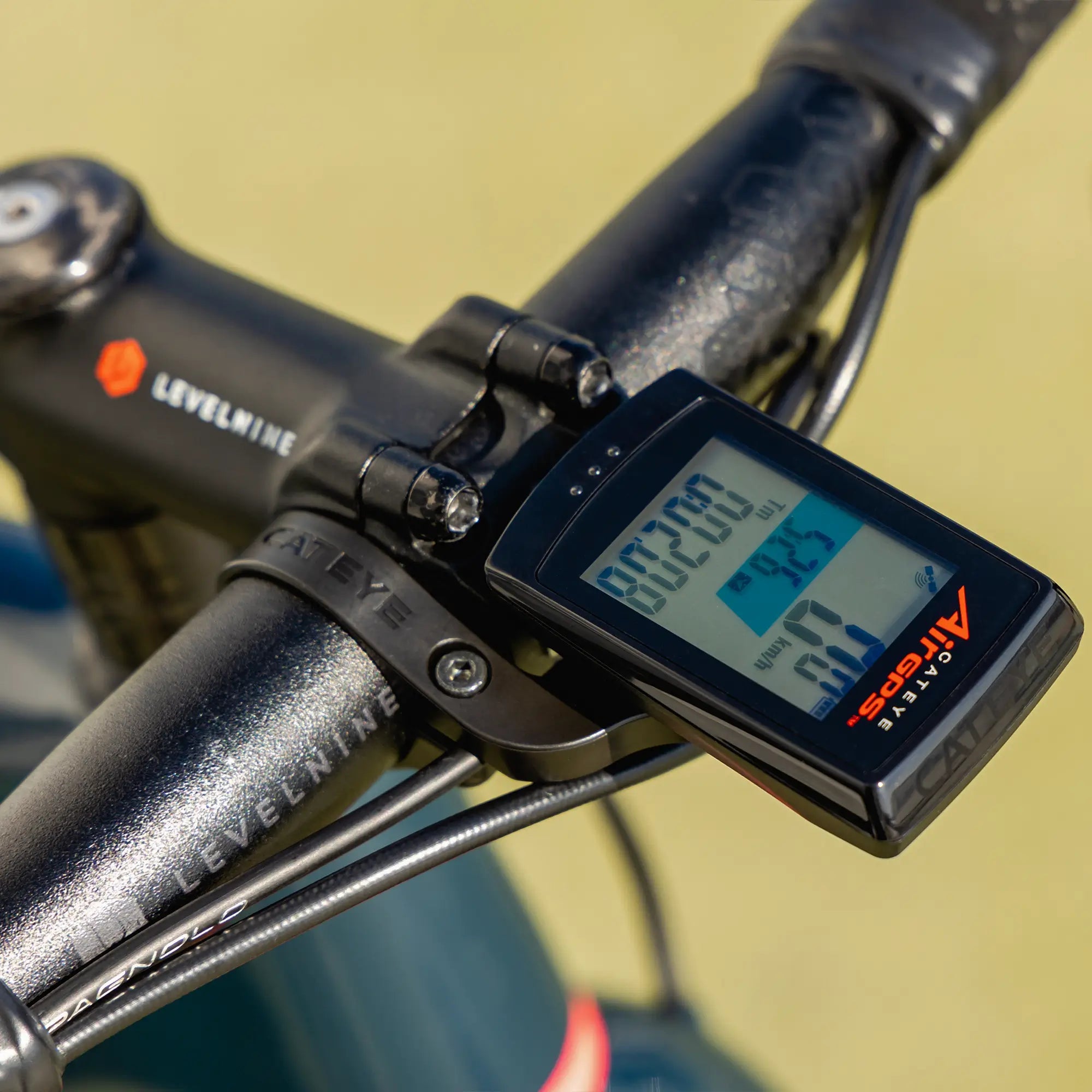 A close-up of CATEYEs AirGPS digital bike computer mounted on a handlebar, displaying speed, distance, and time. The branded handlebar and visible gear cables enhance the GPS accuracy for precise cycling data tracking.