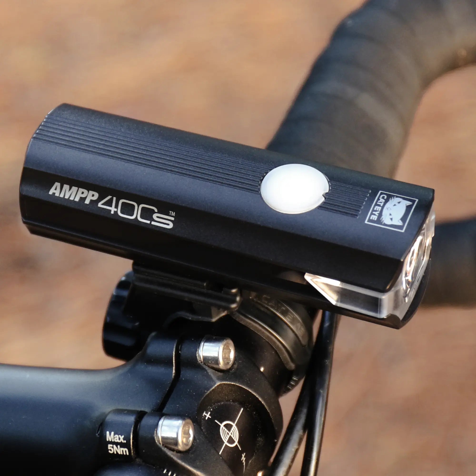 A black CATEYE AMPP400S & ViZ100 bicycle headlight featuring 400 lumens and OptiCube™ lens technology is mounted on bike handlebars, with a blurred outdoor background.