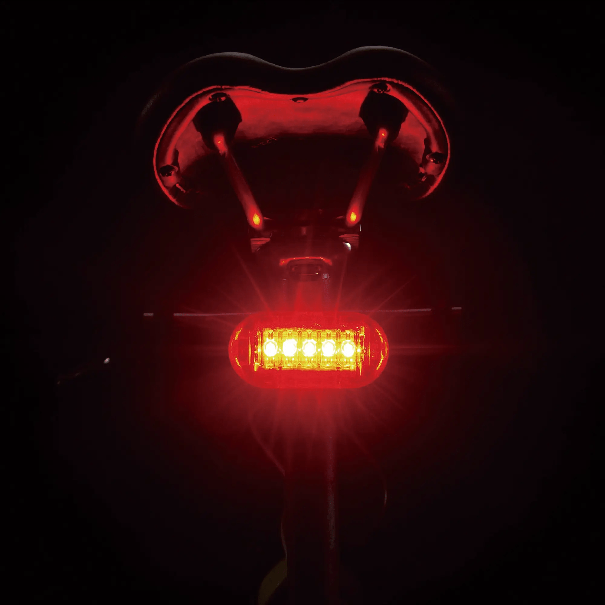 The CATEYE Hl-El160 & OMNI 5 tail light glows brightly in the dark beneath a bike seat, illuminating the saddle and rails to provide 360° visibility.