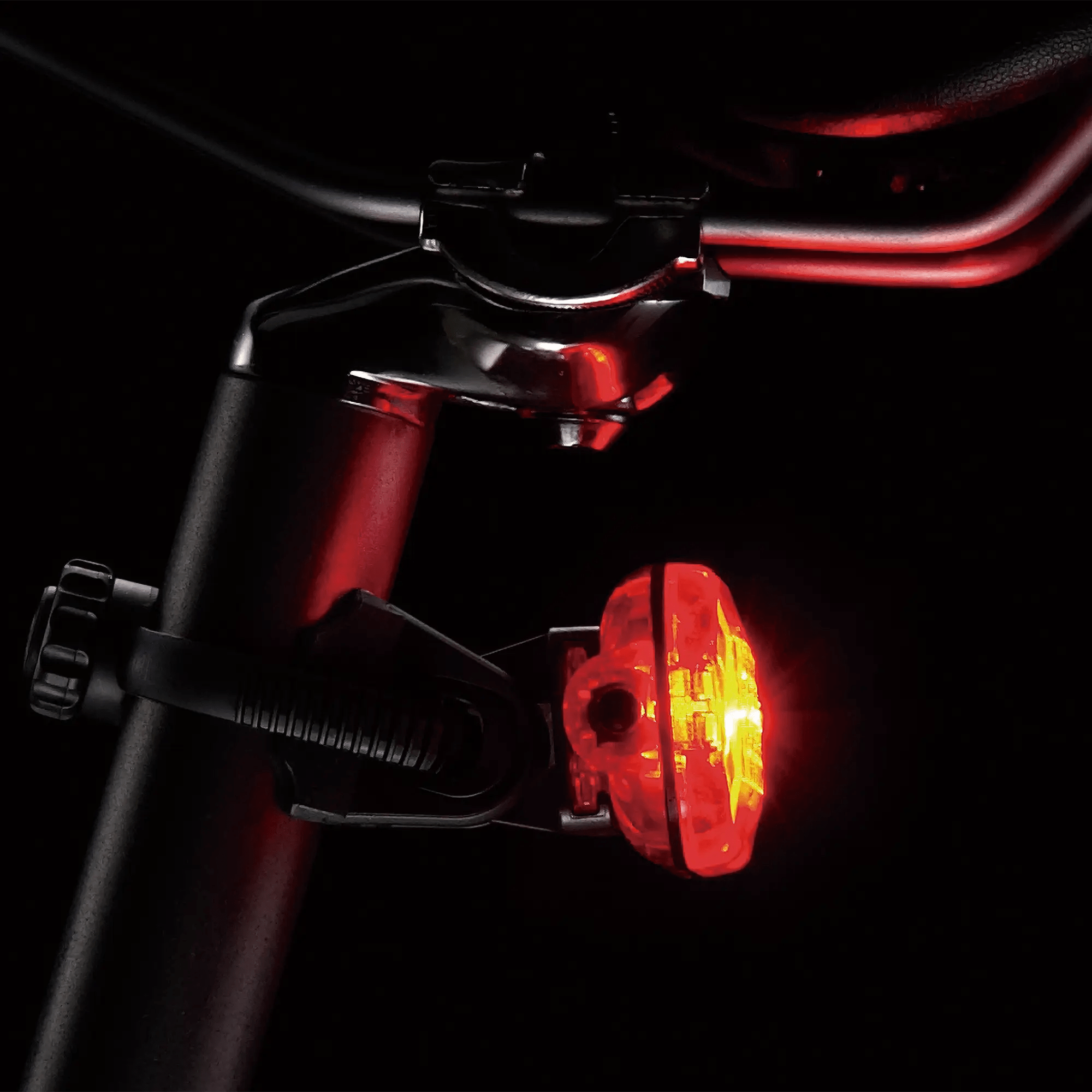 A close-up of the CATEYE Hl-El160 & OMNI 5 red LED bike tail light attached to a seat post, shining brightly in the dark for 360° visibility.