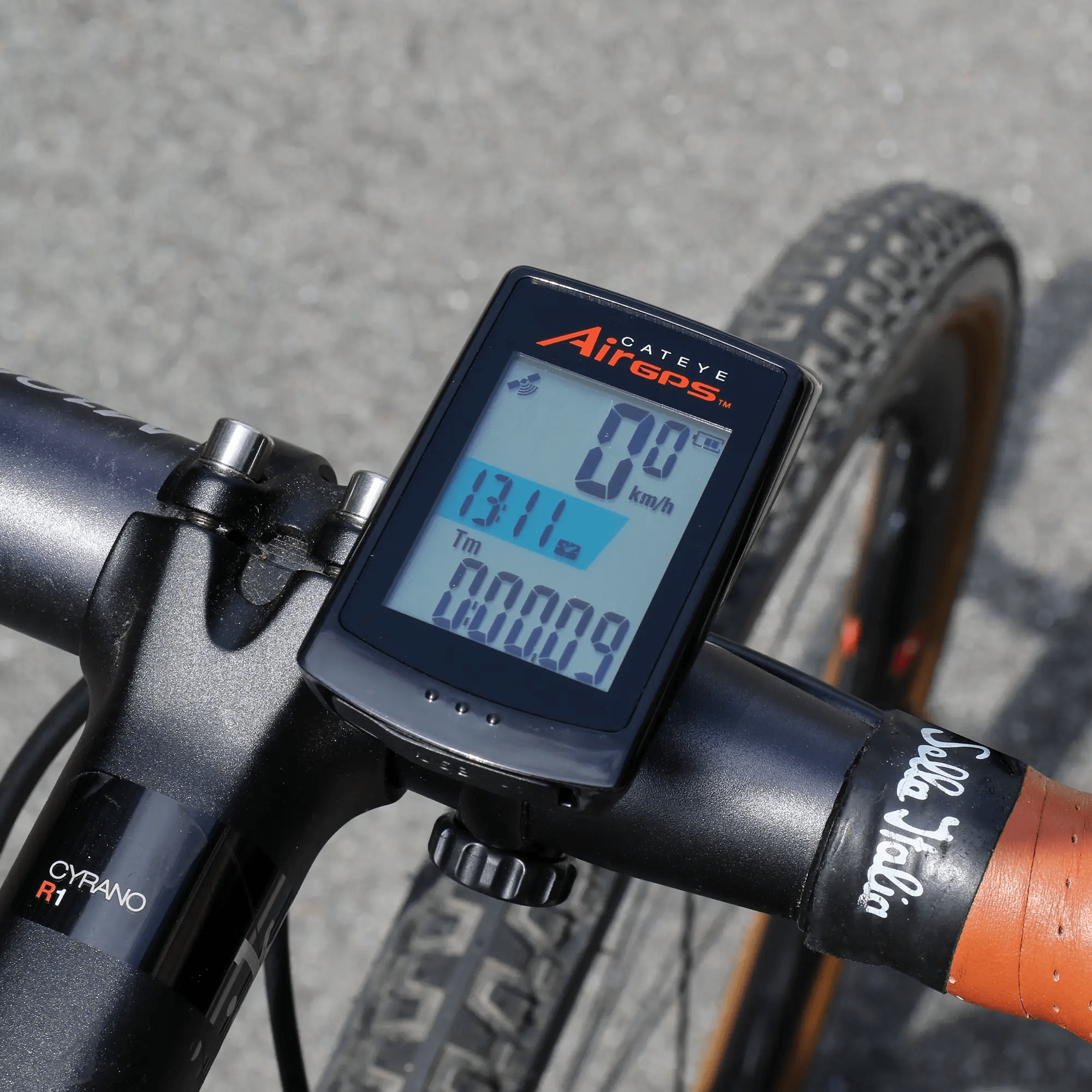 A CATEYE AirGPS bike computer with high GPS accuracy is mounted on the handlebar, showing speed, distance, and time. The bike has a black Cyrano R1 stem, brown-rimmed tires, and syncs with the CATEYE Cycling app.
