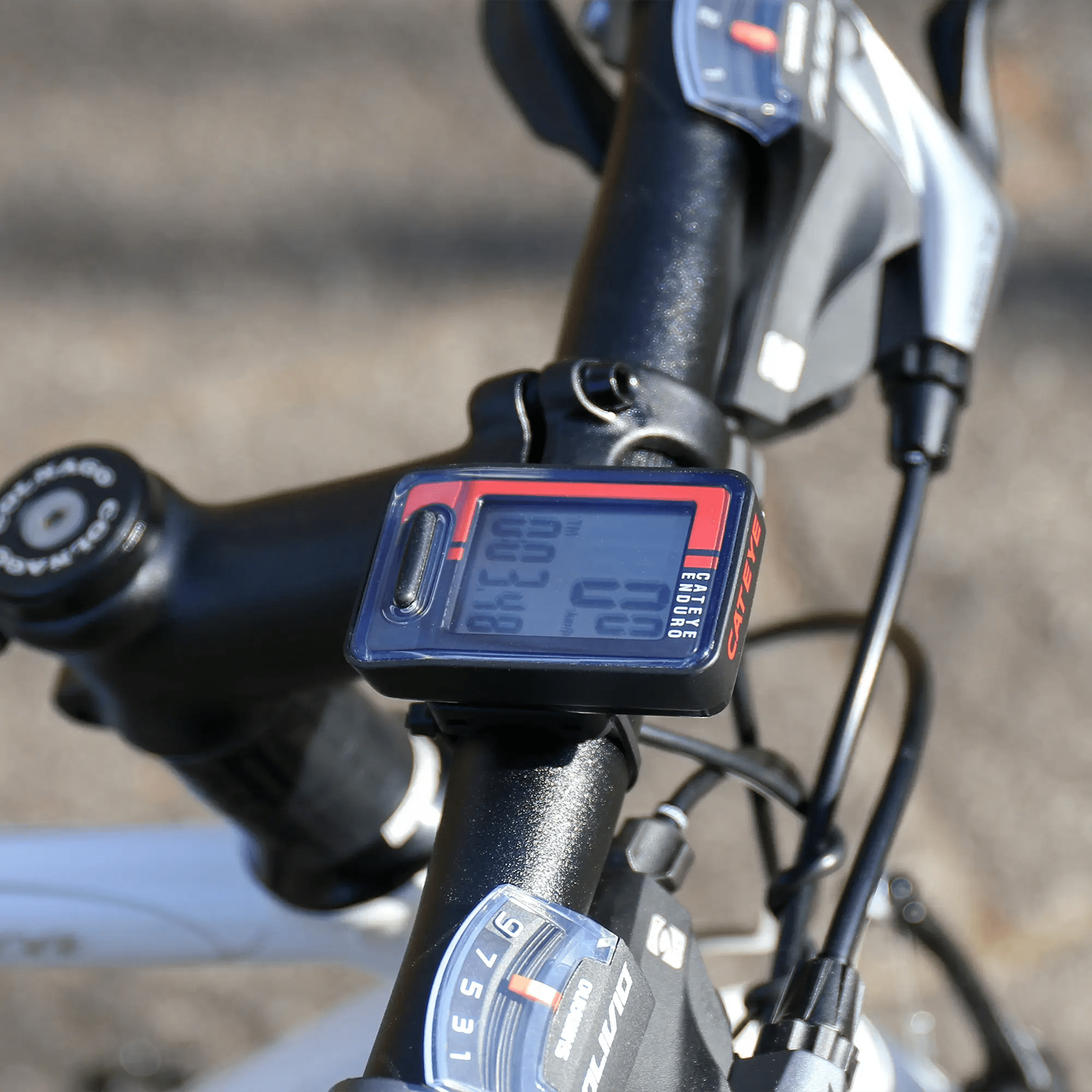 Close-up of a CATEYE Enduro (CPSC) wired computer on a black and white bike handlebar, securely mounted with zip-ties, displaying speed and distance—ideal for adventurous cyclists.