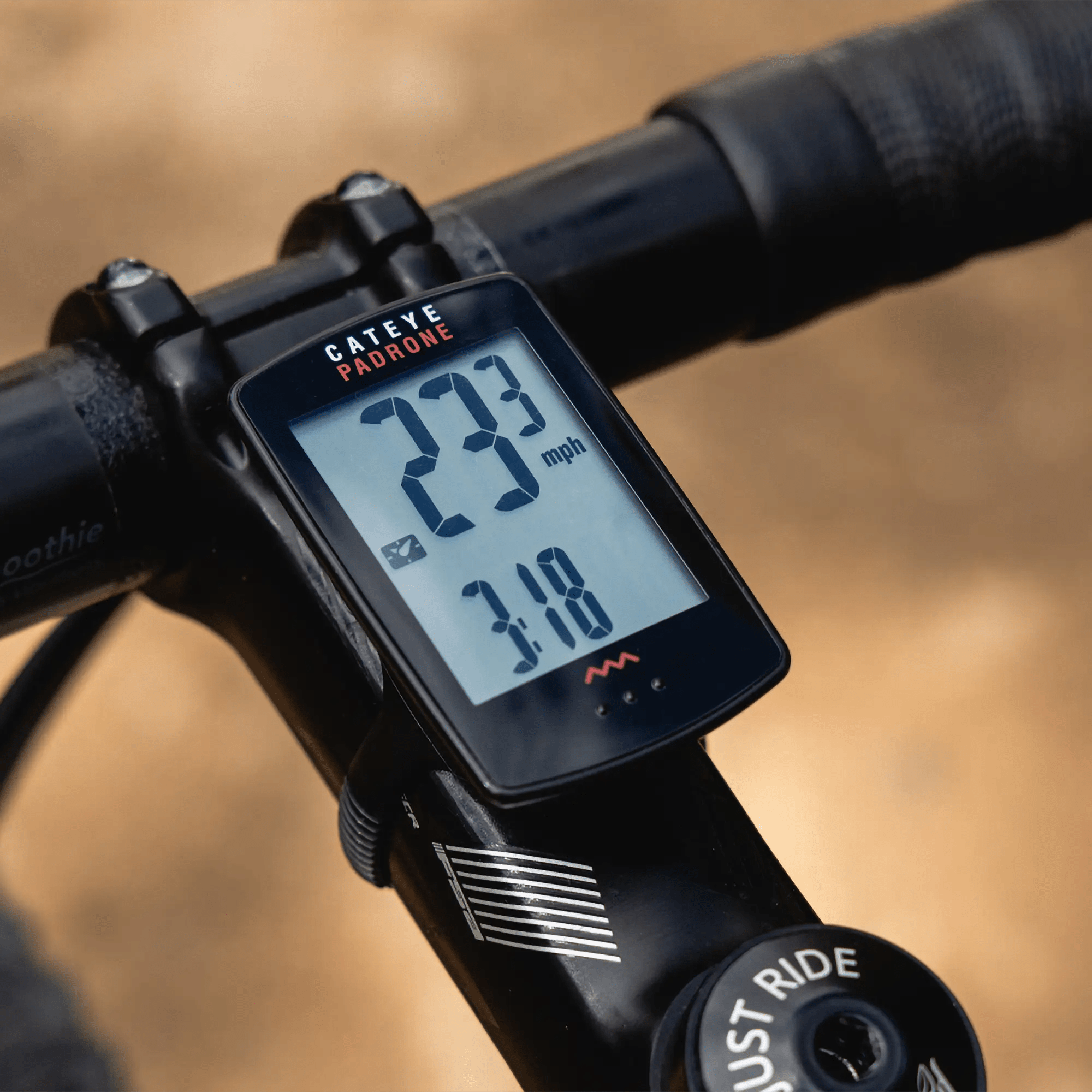 Close-up of a CATEYE Padrone (CPSC) bike computer with large display mounted on handlebars, showing 23.3 mph and a time of 3:18. The blurred background highlights its intuitive ClickTec™ button interface.