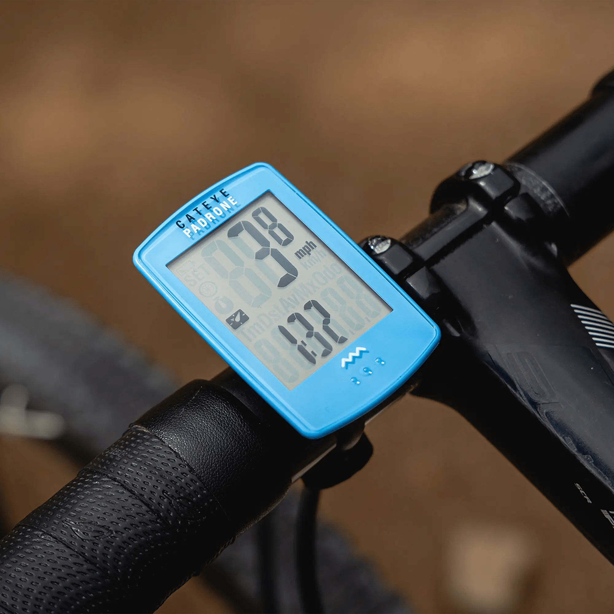 A CATEYE Padrone (CPSC) bike computer with a large display is mounted on a handlebar, showing 9 mph speed and 13.0 miles traveled, easily navigated using the ClickTec™ button interface.