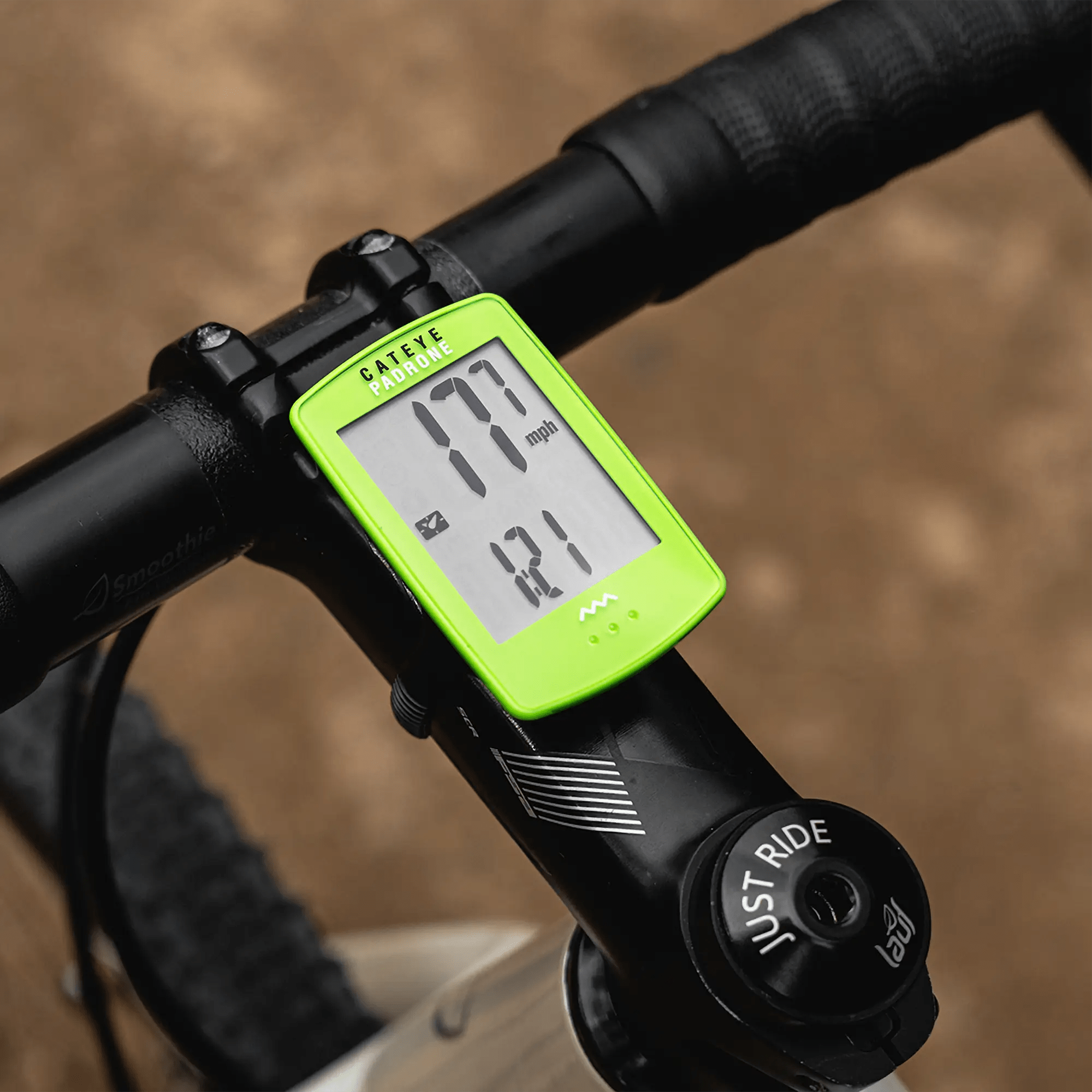 A green CATEYE Padrone (CPSC) bike computer with a large display is mounted on a handlebar, showing 17.7 mph speed and 121 cadence as the bike rides along a dirt path.