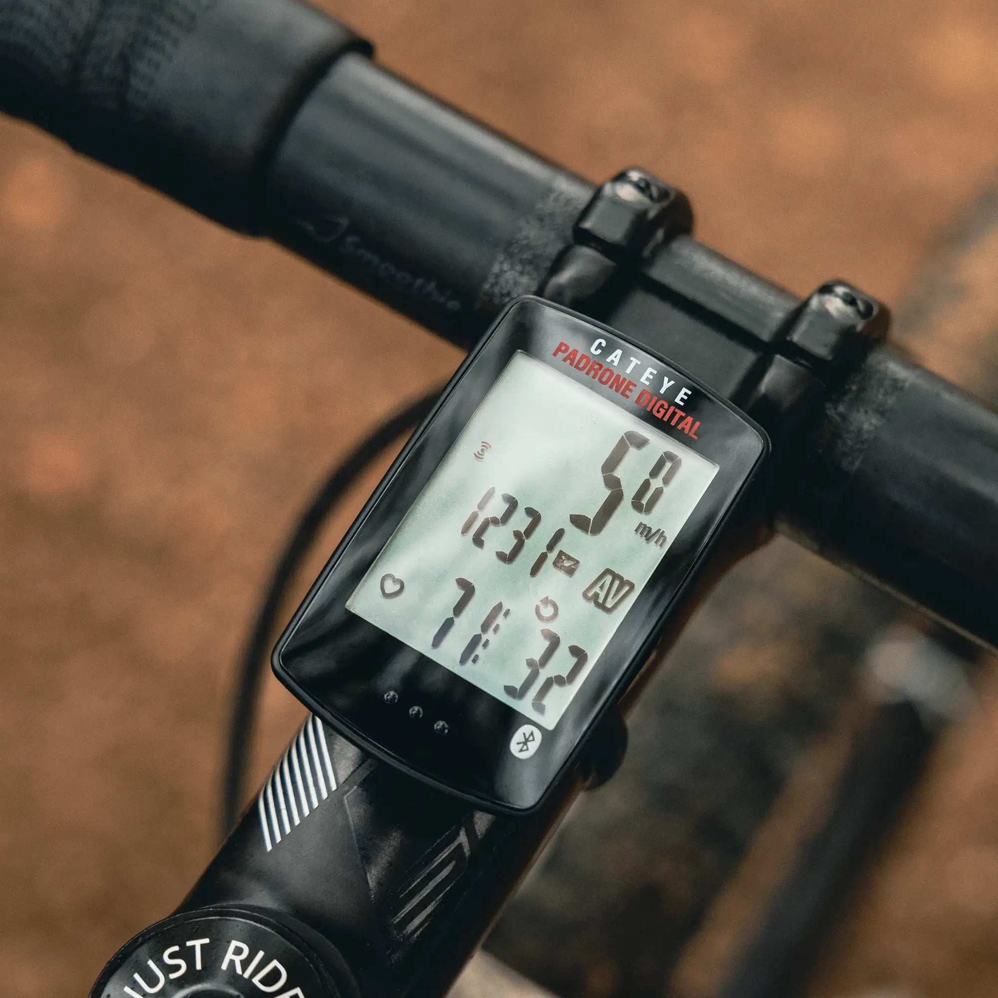 A close-up of a CATEYE Padrone Digital (CPSC) bike computer on a handlebar, showing speed, average speed, distance, and time from wireless sensors on its clear display.