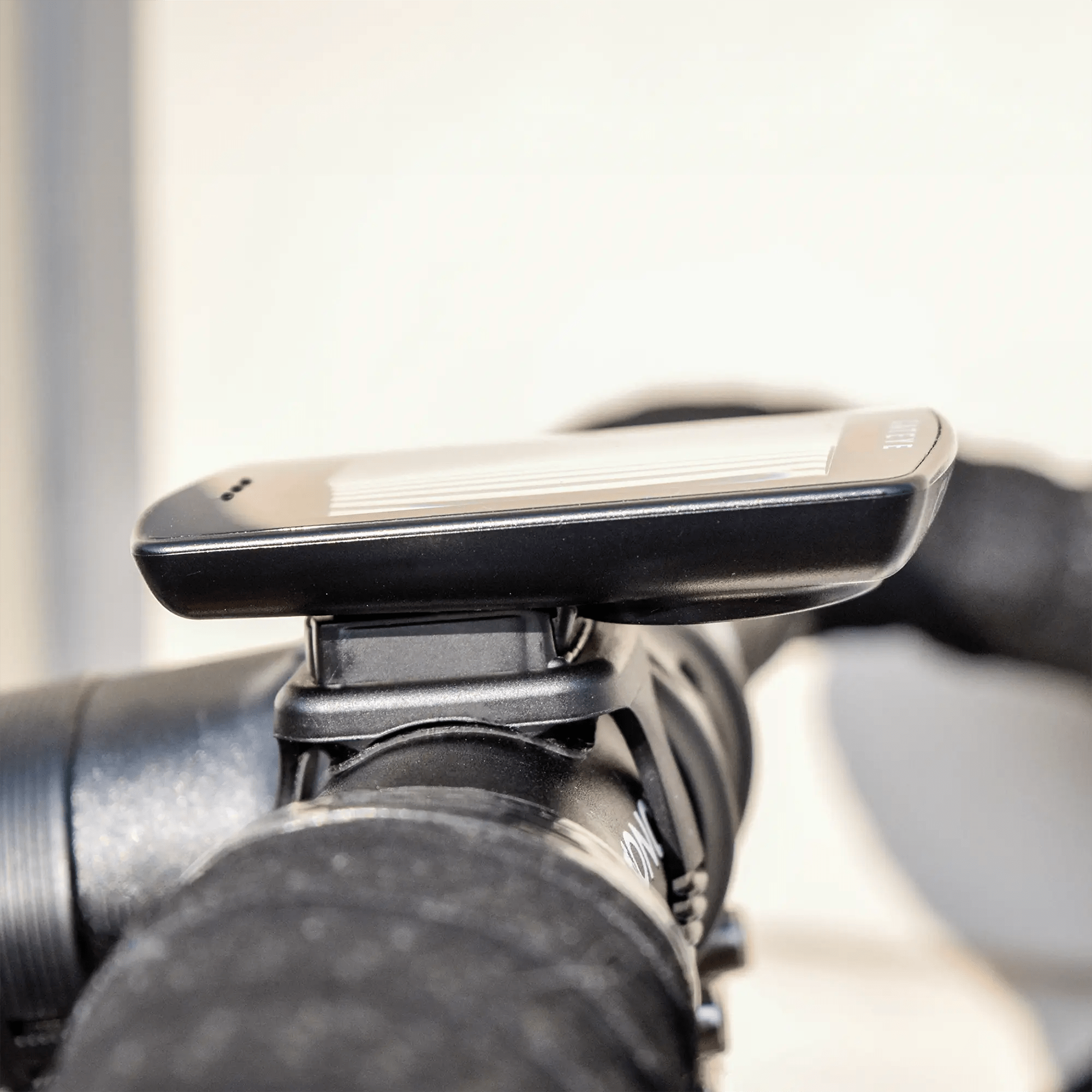 A close-up of the CATEYE Padrone Plus (CPSC) cycling computer with a large display and adjustable backlight, mounted on bicycle handlebars against a blurred background.