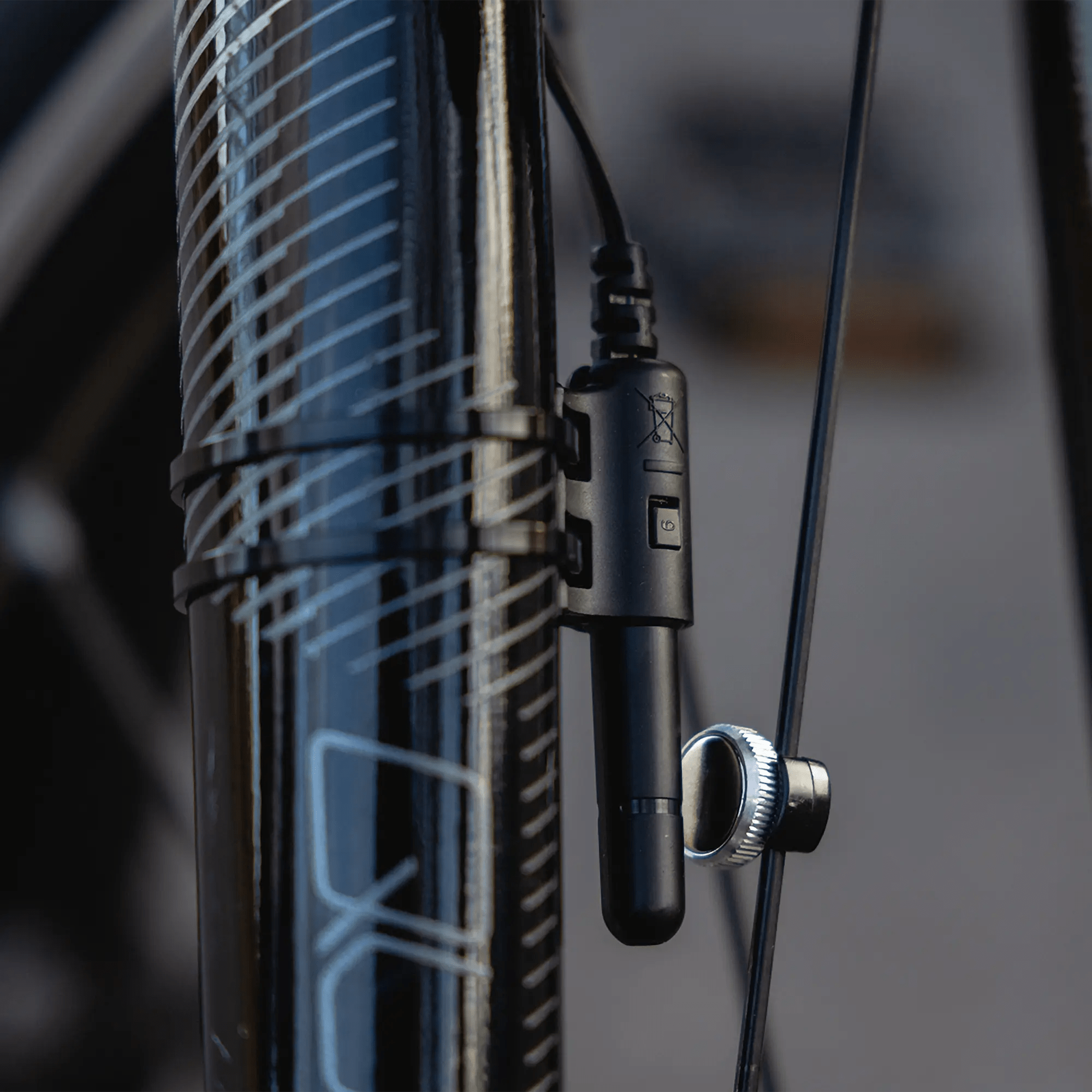 Close-up of a black bicycle fork featuring the CATEYE Velo 9 sensor and wire, secured with zip ties near the wheel’s spoke and magnet. This entry-level bike computer is ideal for novice cyclists.