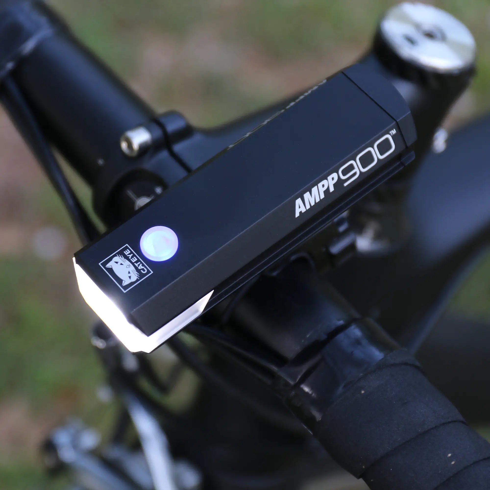 A close-up of a CATEYE AMPP900 bicycle headlight with OptiCube™ lens technology, mounted on handlebars and emitting a 900 lumen white beam.