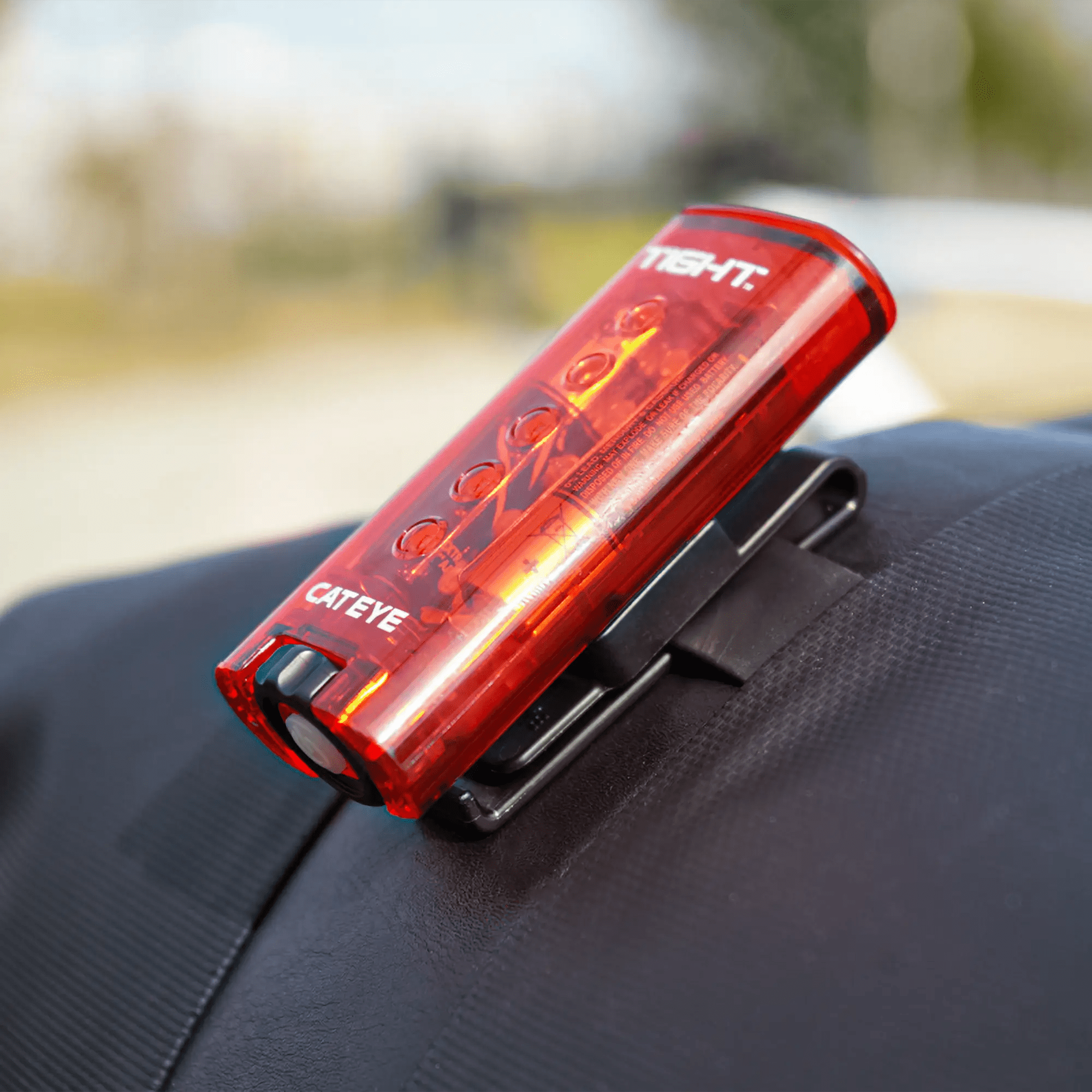 A red CATEYE C-2 Clothing Clip is attached to a black strap on gear, with a blurred outdoor background.