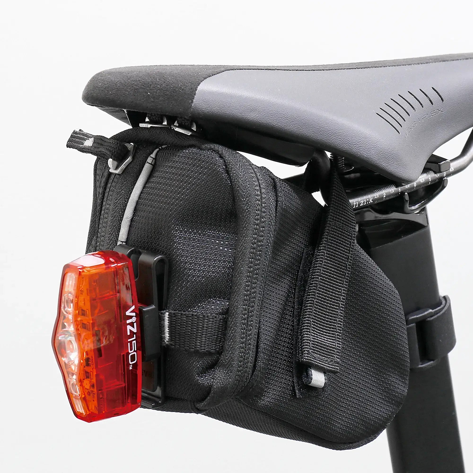 A black bicycle saddle with a small black saddlebag attached underneath. A CATEYE C-2 Clothing Clip is clipped to the back of the saddlebag. The background is plain white.