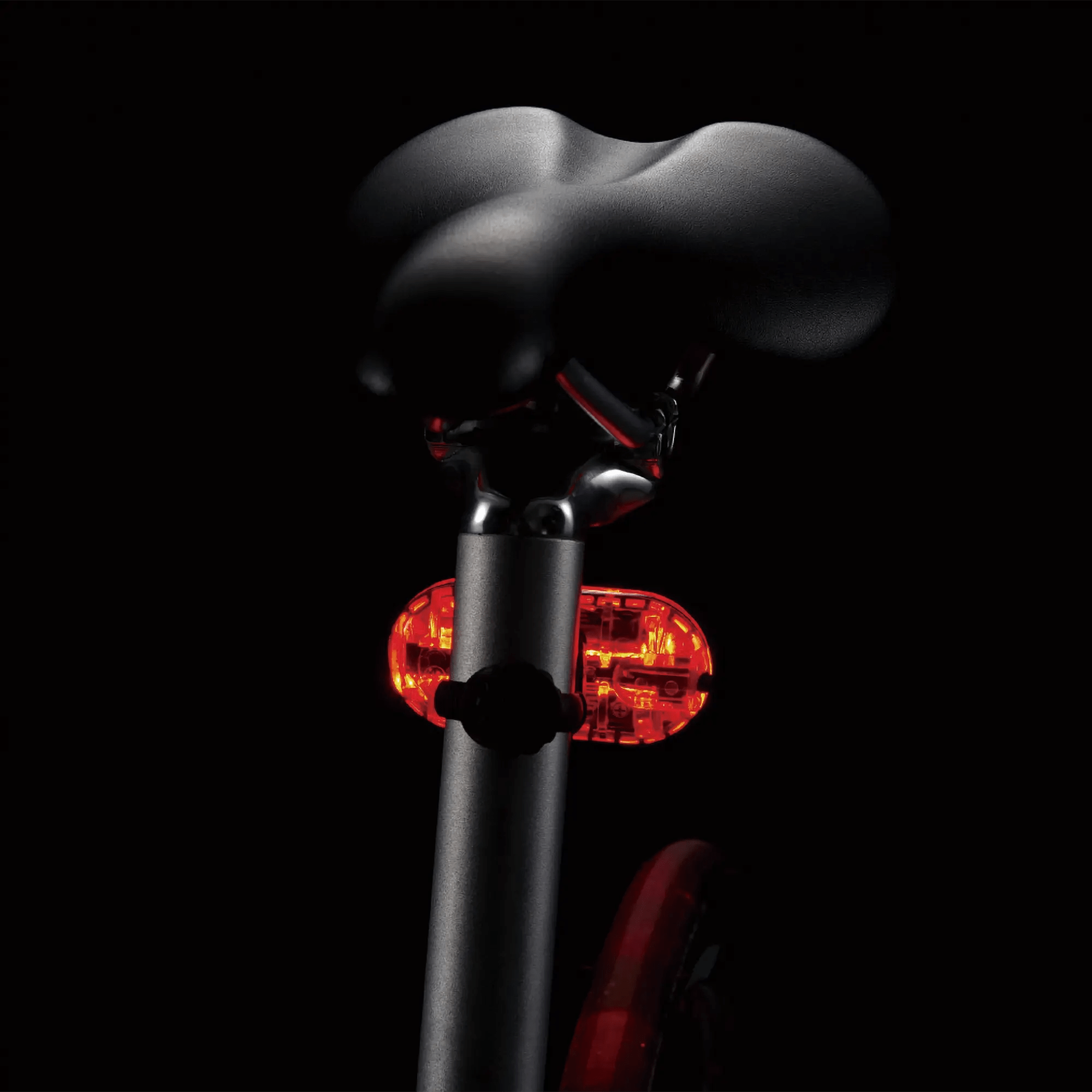 Close-up of a bicycle seat showcasing the CATEYE OMNI 5 rear light with OptiCube™ lens, emitting a bright red safety glow and delivering 360-degree visibility against a dark background.