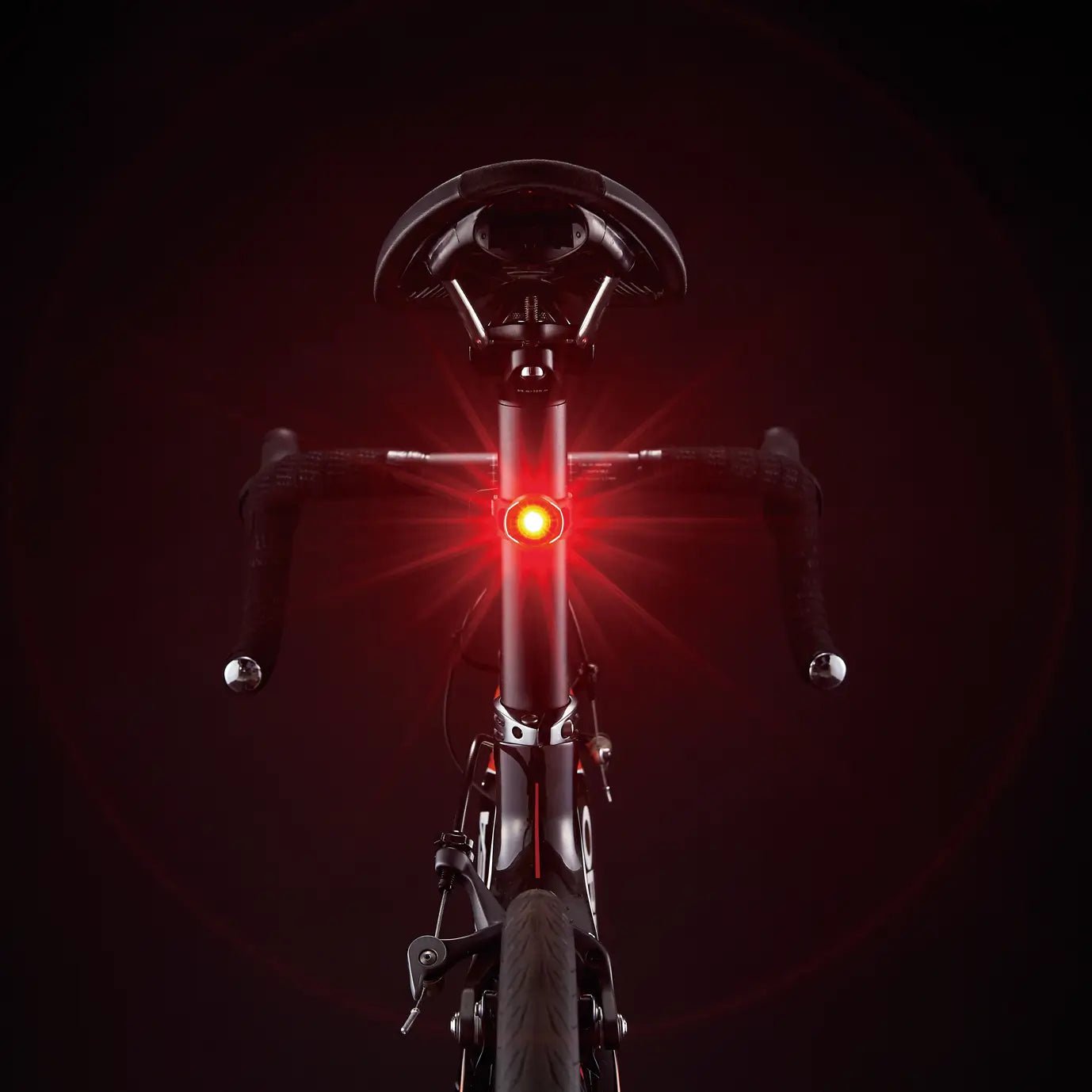 The CATEYE ORB, shown from behind against a dark background, features a bright red safety light beneath the seat with flared rays for visibility. Its lightweight alloy chassis enhances its modern design.