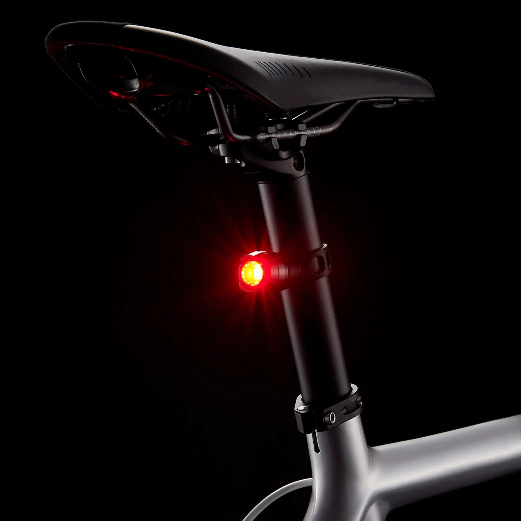 A close-up of the CATEYE ORB bicycle seat and seat post shows a bright red rear safety light with multiple lighting modes, illuminated against a black background.