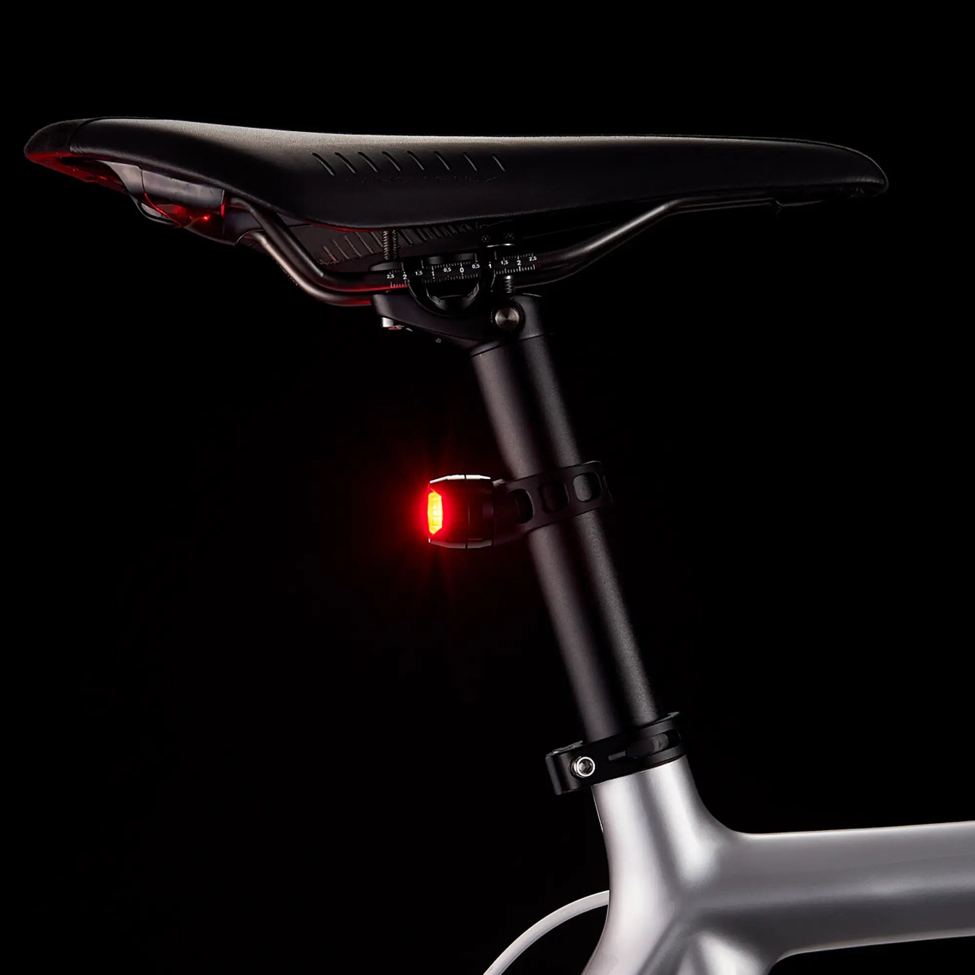 A close-up of the CATEYE ORB showcases its red rear safety light illuminated on a bicycle seat and seat post, set against a black background. Its lightweight alloy chassis and multiple lighting modes enhance night visibility.