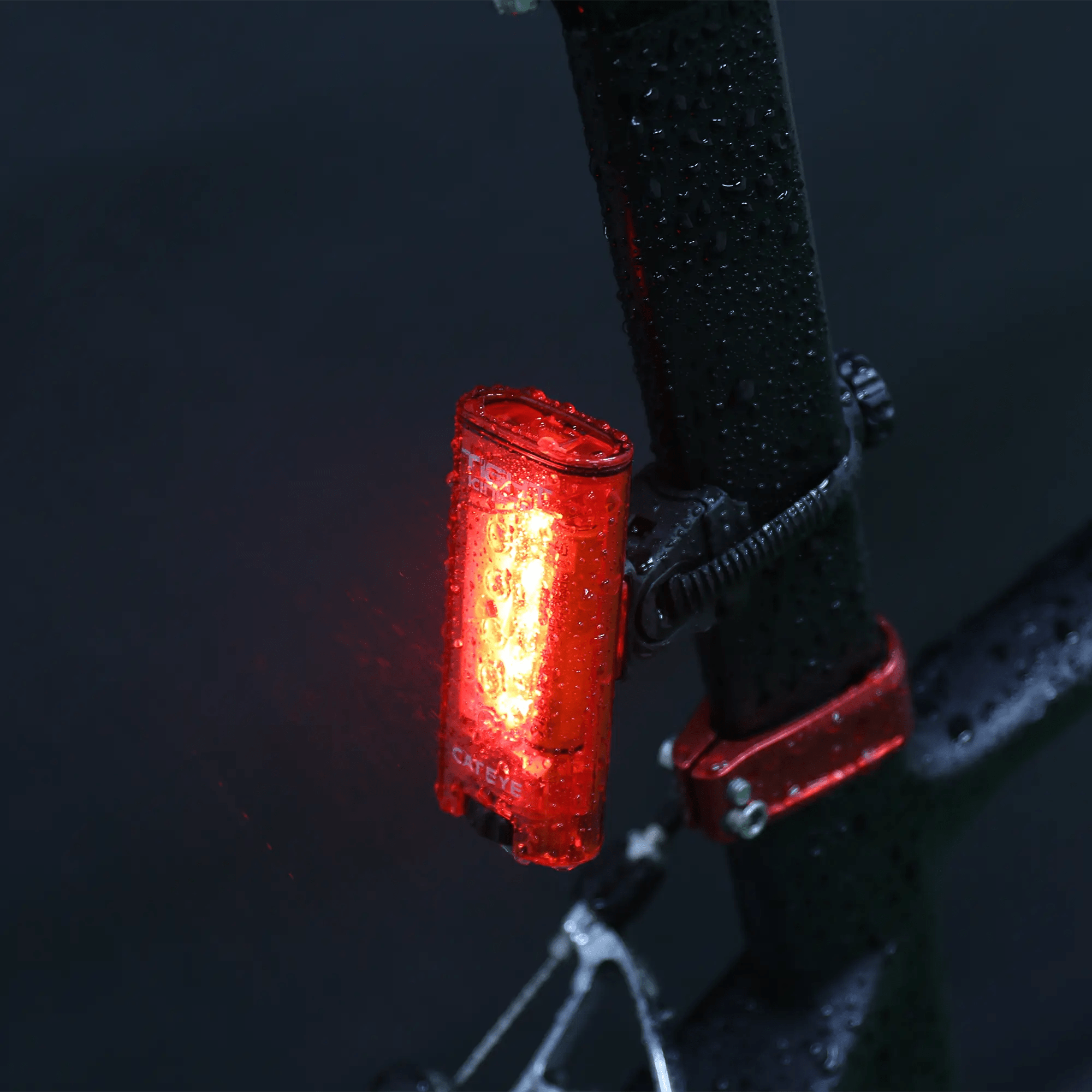The CATEYE Tight Kinetic glows brightly on a wet bicycle frame against a dark background—its IPX7 waterproof rating ensures reliable performance in any weather.