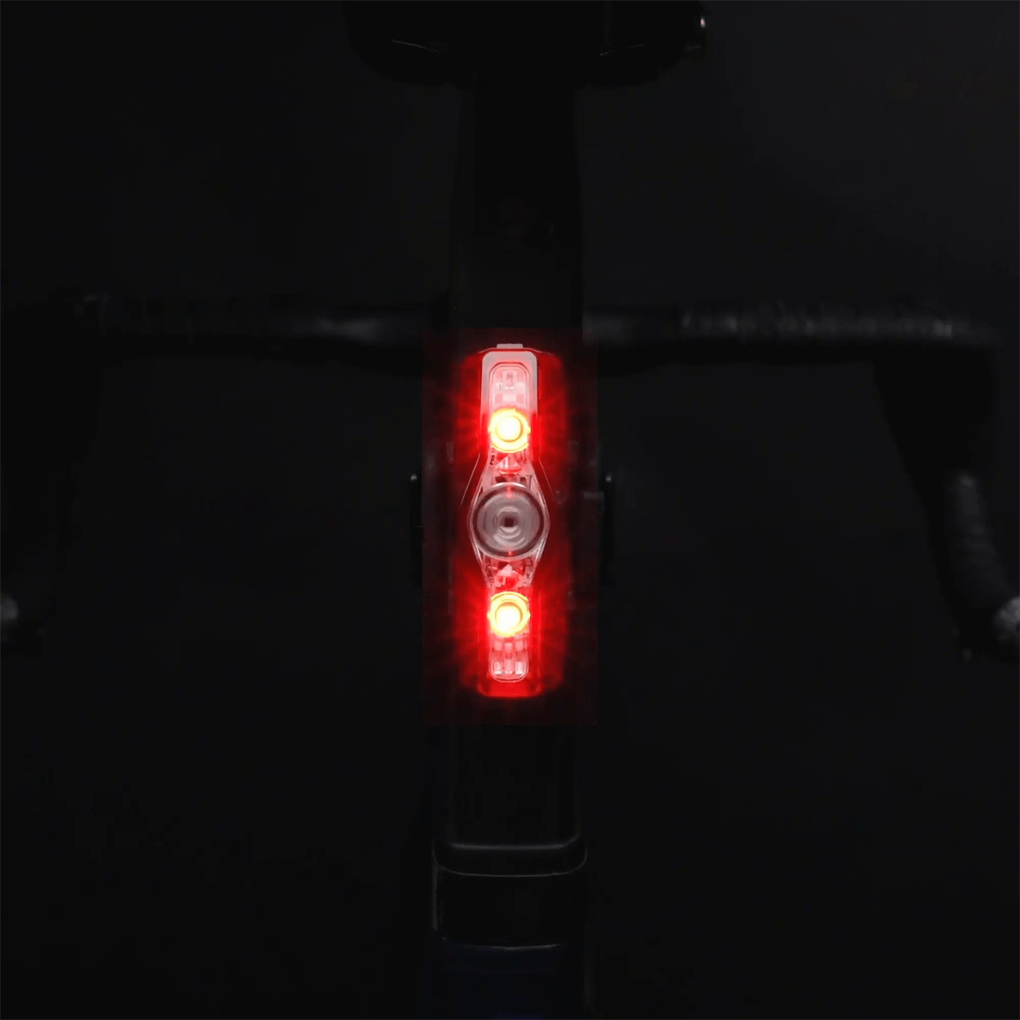 A close-up of a bicycle handlebar in the dark, featuring CATEYE’s ViZ150 (USB-C) rear light with OptiCube™ lens technology glowing bright red at the center, illuminating the scene against a mostly black background.