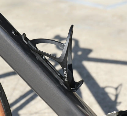 A CATEYE BC-400 Bottle Cage in black is attached to a bike frame, providing universal compatibility, with a blurred outdoor background.