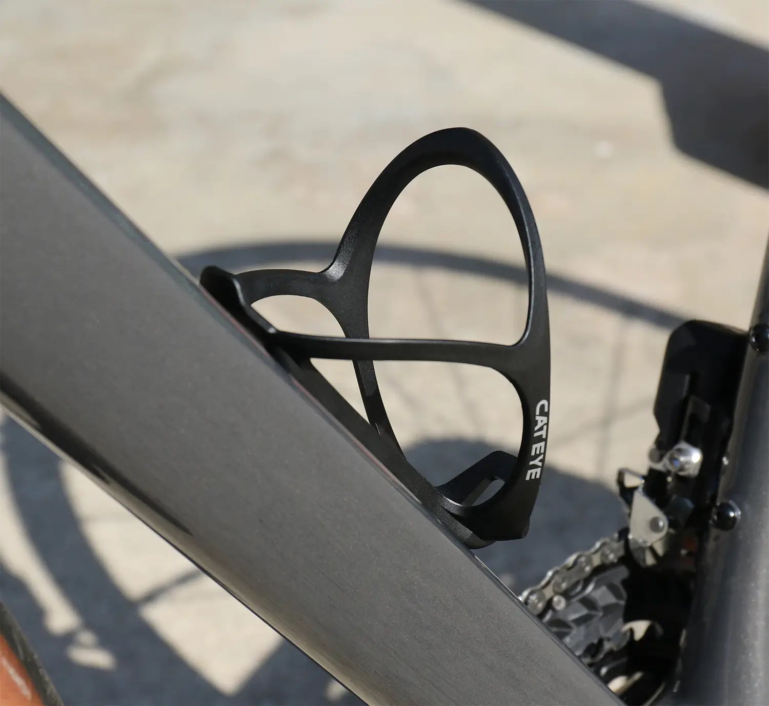 Close-up of a CATEYE BC-400 Bottle Cage mounted on a bike frame, with the chain and gear mechanism partially visible in the background.
