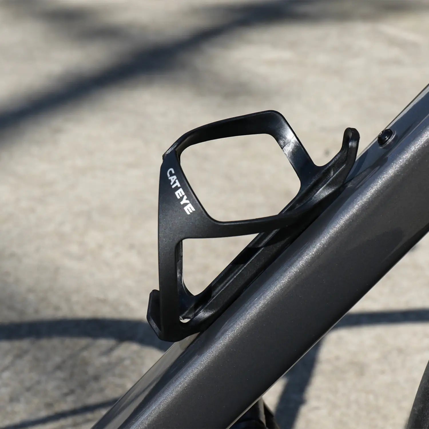 A black CATEYE BC-500 Bottle Cage is mounted on a gray bike frame with blurred pavement in the background—ideal for easy bottle access during your bikepacking adventures.