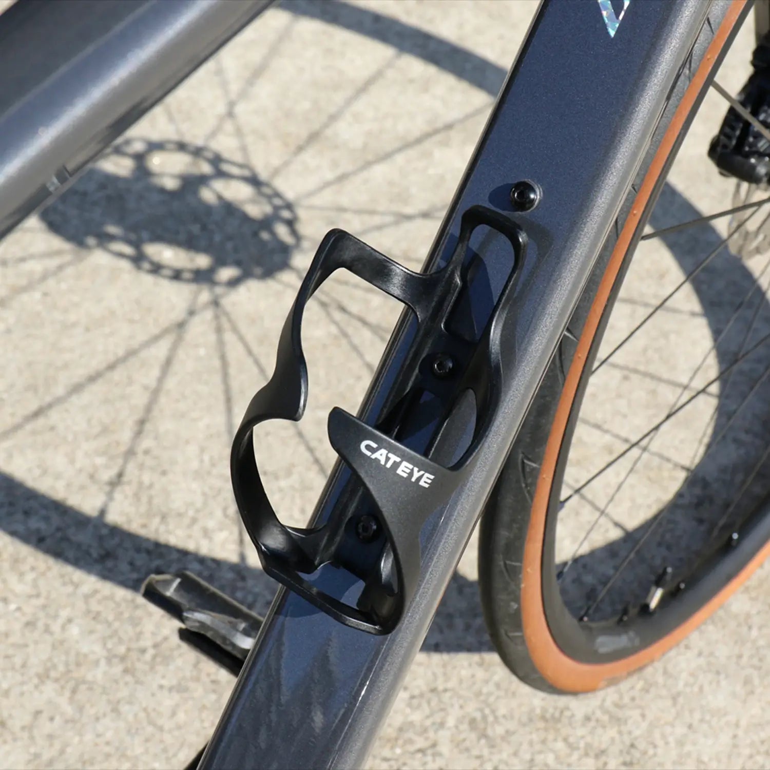 Close-up of a black CATEYE BC-500 Bottle Cage mounted on a bike frame, with the tire and disc brake visible in the background—perfect for bikepacking trips.