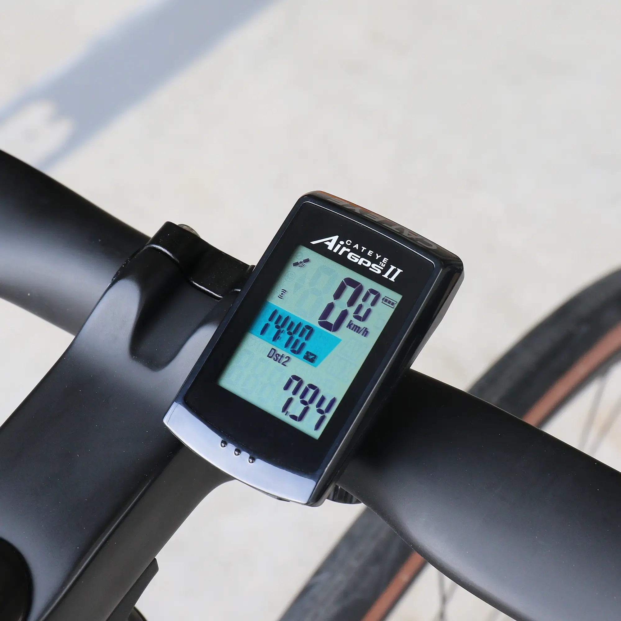 A close-up of a CATEYE AirGPS II bike computer on handlebars shows a digital screen with GPS accuracy, displaying speed (0.0 km/h), distance (144.0 km), and time (9:34).