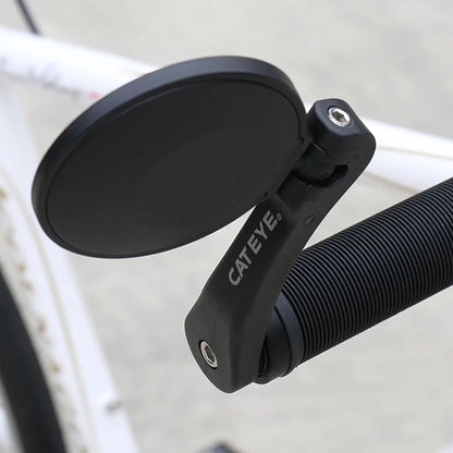 A close-up of a black CATEYE BM-600 Handlebar Mirror with a stainless steel lens, mounted on the handlebar of a white bicycle, enhancing rear visibility against a blurred background.