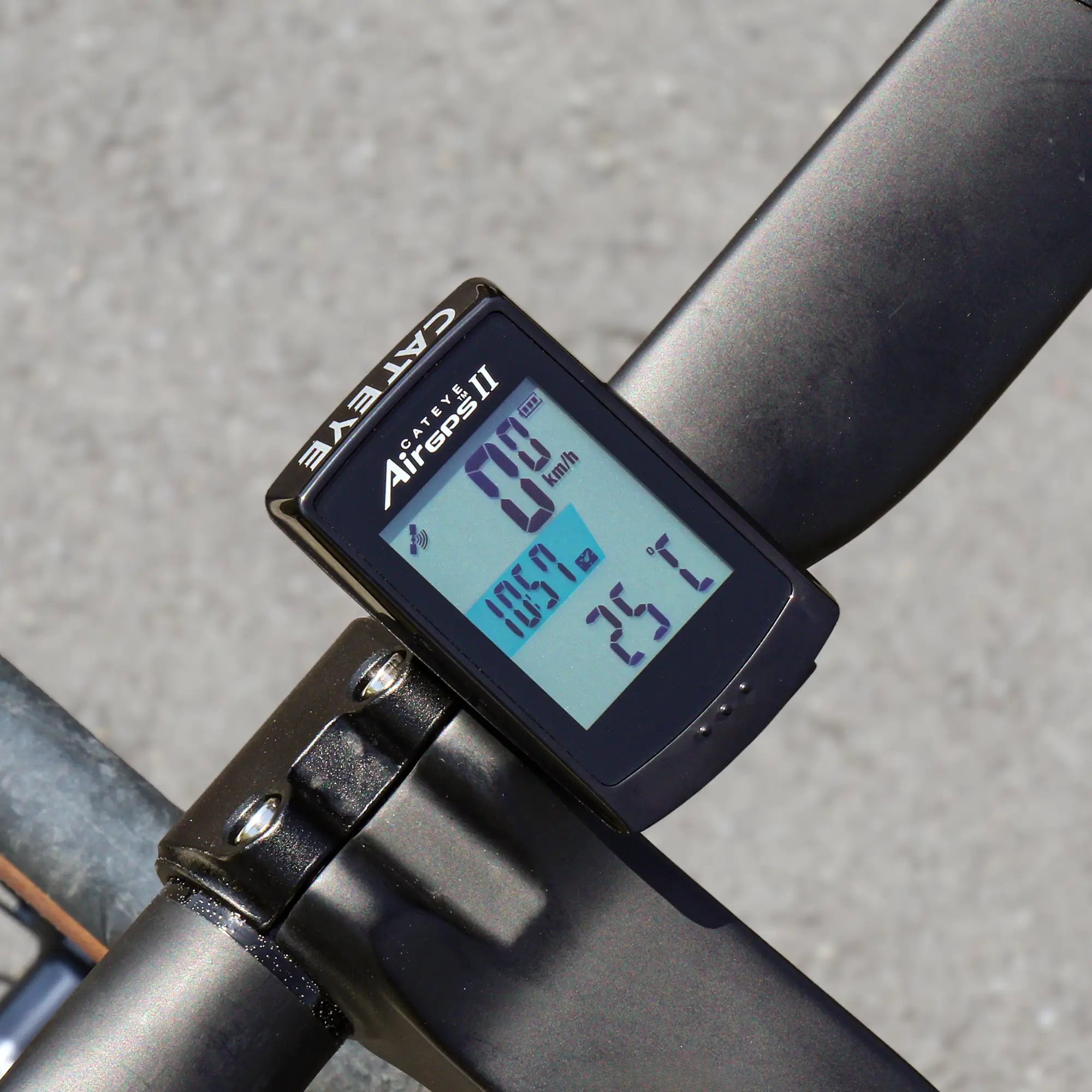A close-up shows the CATEYE AirGPS II bike computer mounted on handlebars, displaying speed, distance, and temperature with precise GPS accuracy. The background features a blurred gray pavement surface.