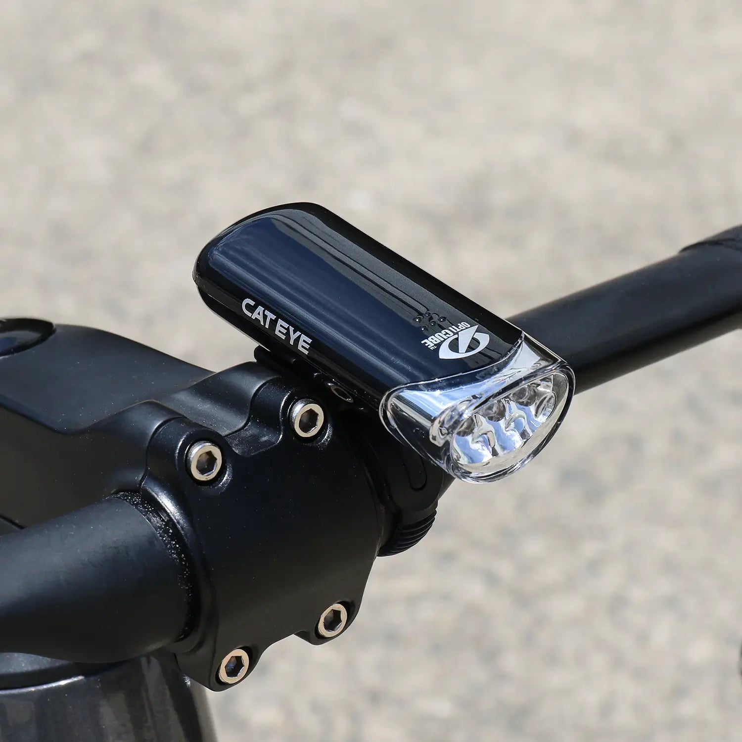 A CATEYE HL-EL135N black bicycle headlight with three LEDs and OptiCube lens is mounted to handlebars using a FlexTight H-34N bracket, set against a blurred outdoor background.