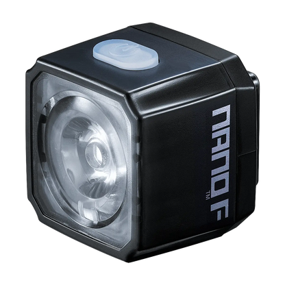The CATEYE NANO100 F is a compact, black, cube-shaped 100-lumen bike light with a clear front lens and gray top power button, offering daytime front safety and visibility.