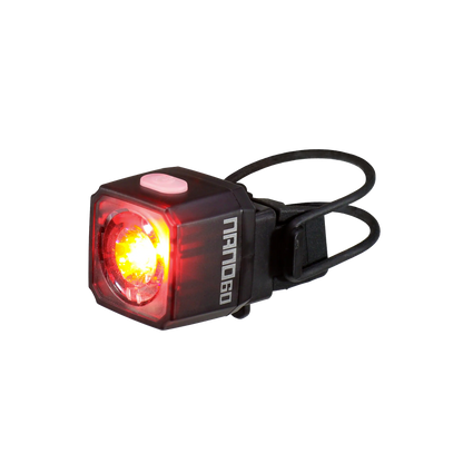 A compact, black, rectangular CATEYE NANO60 bike tail light with a red LED, pink top button, and rubber mounting strap. USB-C rechargeable for enhanced daytime visibility, with NANO60 printed on the side.